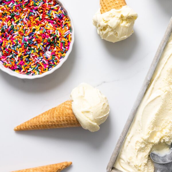 Top down view of vanilla ice cream in container with ice cream scooped into an ice cream cone with sprinkles in white container