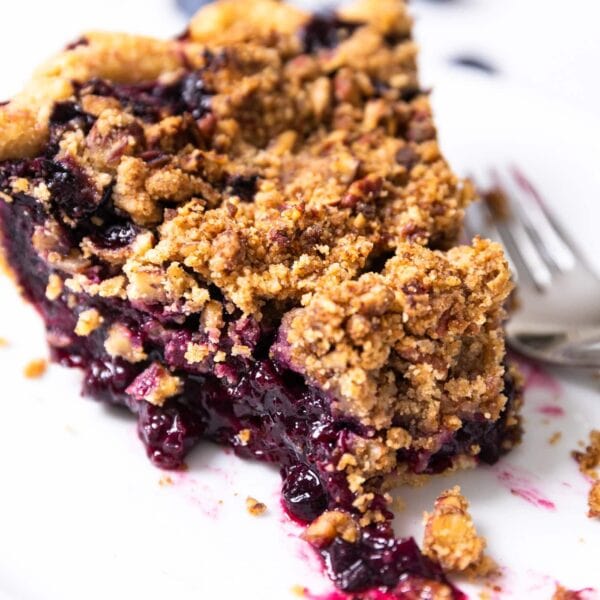 Close up picture of slice of blueberry pie sitting on white plate with fork on plate