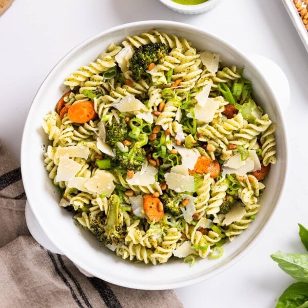 Top down view of white bowl filled with cooked pasta along with pieces of carrot and broccoli sitting on white countertop with towel underneath