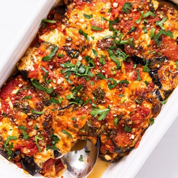 Top down view of white casserole dish filled with red colored eggplant parmesan with cheese and green herbs all over the top sitting on white countertop