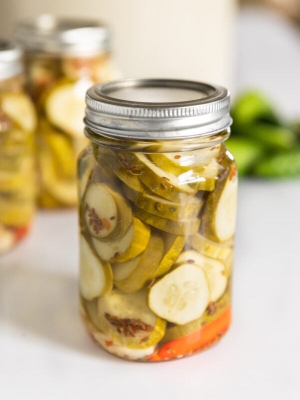 Glass canning jar with metal lid and ring on top with slices of spicy dill pickles inside sitting on white countertop
