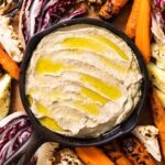 Top down view of black cast iron skillet filled with Baba ganoush drizzled on top with olive oil sitting on wood board filled with grilled vegetables