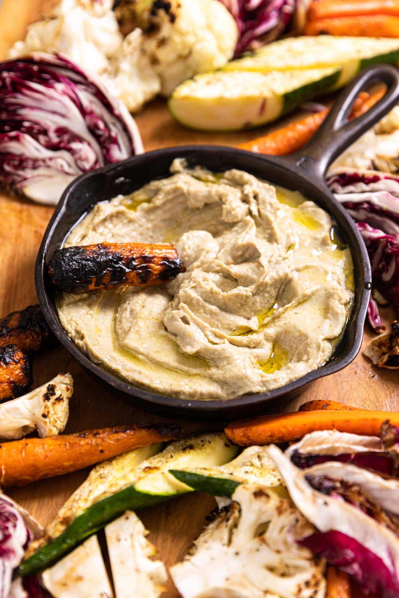 Skillet filled with baba ganoush with grilled carrot scooping up a serving.