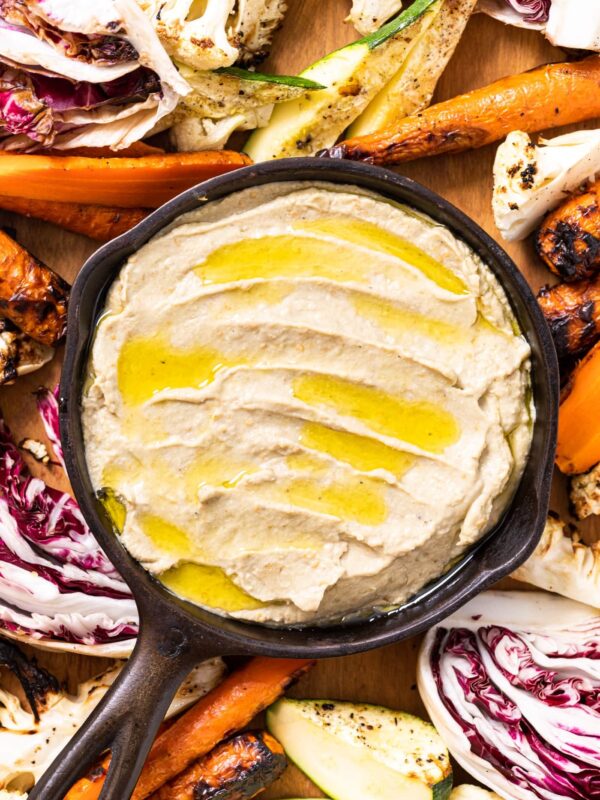 Top down view of small cast iron skillet holding light brown colored Baba ganoush with drizzled olive oil over the top amongst grilled vegetables