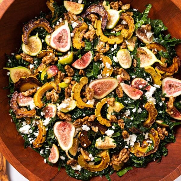 Top down view of hearty kale salad in wooden bowl topped with figs and squash and feta cheese on white countertop