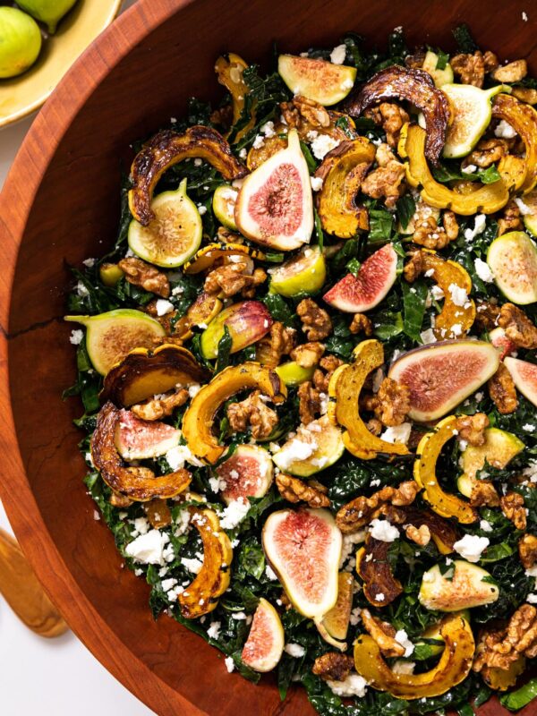 Top down view of large wooden bowl filled with kale salad topped with figs, squash, walnuts, and crumbled white feta