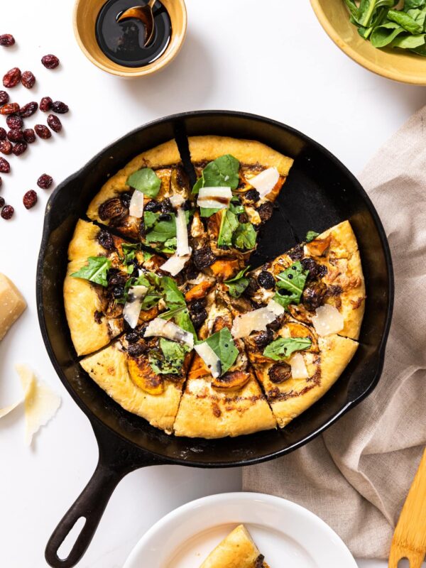 Top down view of rustic pizza sitting in cast iron skillet topped with arugula all on white countertop