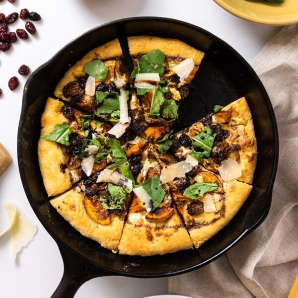 Top down view of black cast iron skillet sitting on white countertop with pizza in skillet topped with arugula