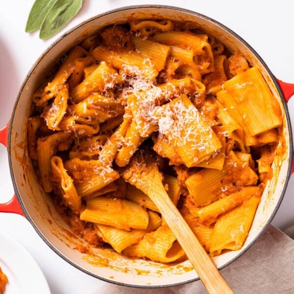 Top down view of large kettle sitting on white countertop filled with orange colored squash pasta with wooden spoon inside
