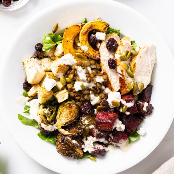 Top down view of white plate filled with a harvest bowl filled with chicken, roasted vegetables, and lentils all on a bed of green lettuce