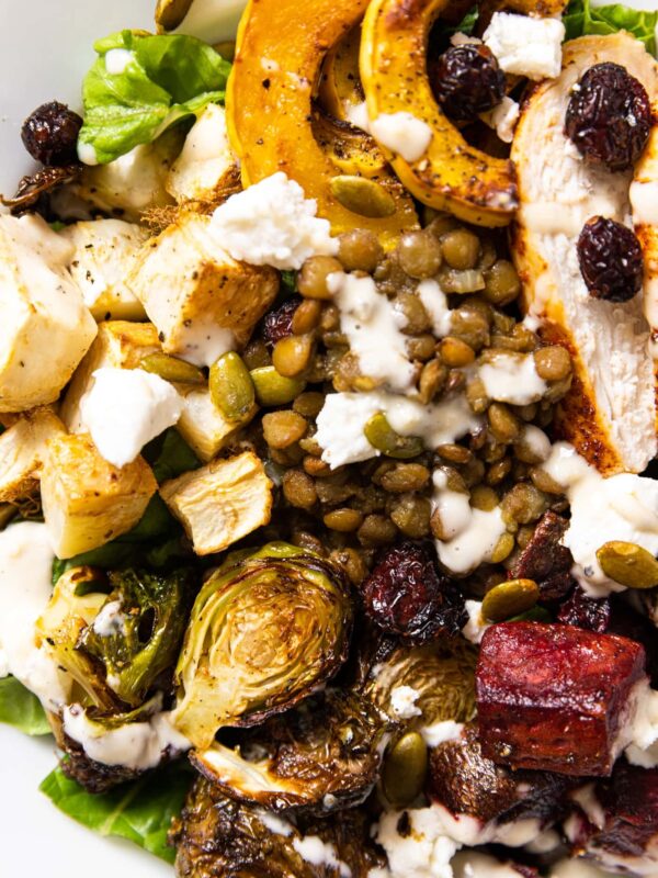 Top down view of white bowl holding lettuce as a base with roasted vegetables all over the top along with lentils and a creamy dressing