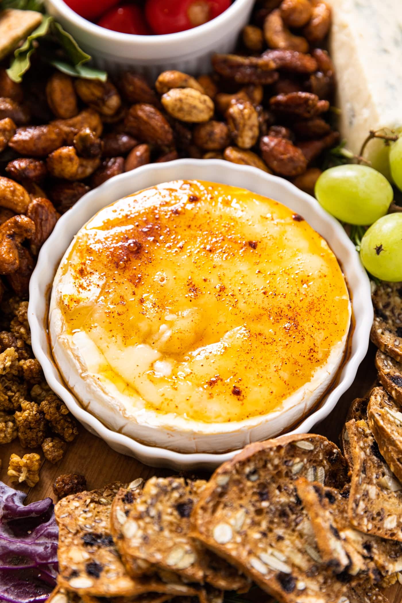 A round white bowl filled with a circle of baked brie with charcuterie all around.