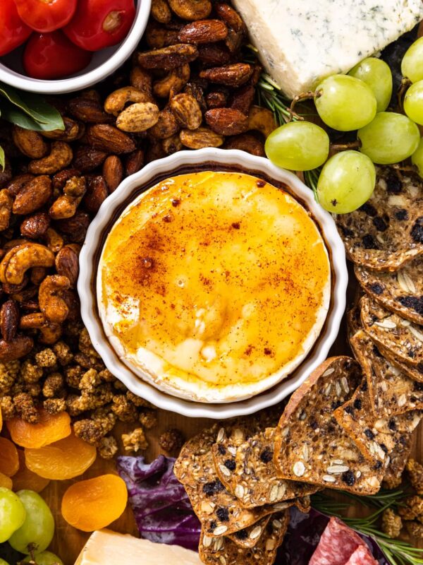 Top down view of small white bowl sitting on charcuterie board filled with baked Brie with yellow colored honey and chipotle on top
