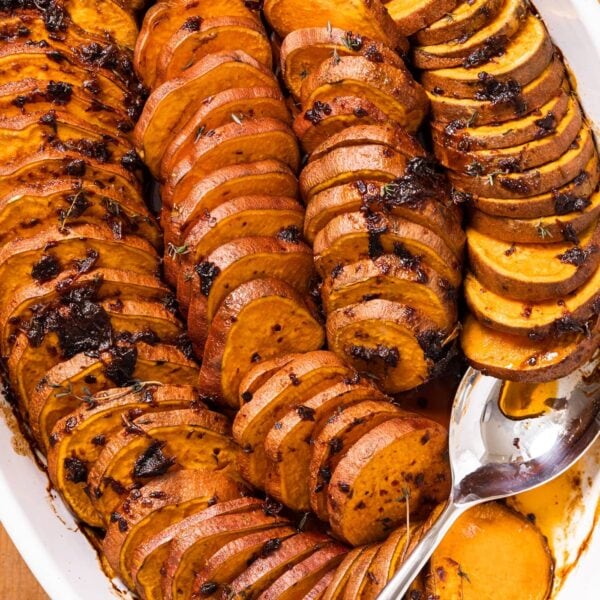 Top down view of white baking pan filled with slices of sweet potatoes covered with chipotle sauce and thyme