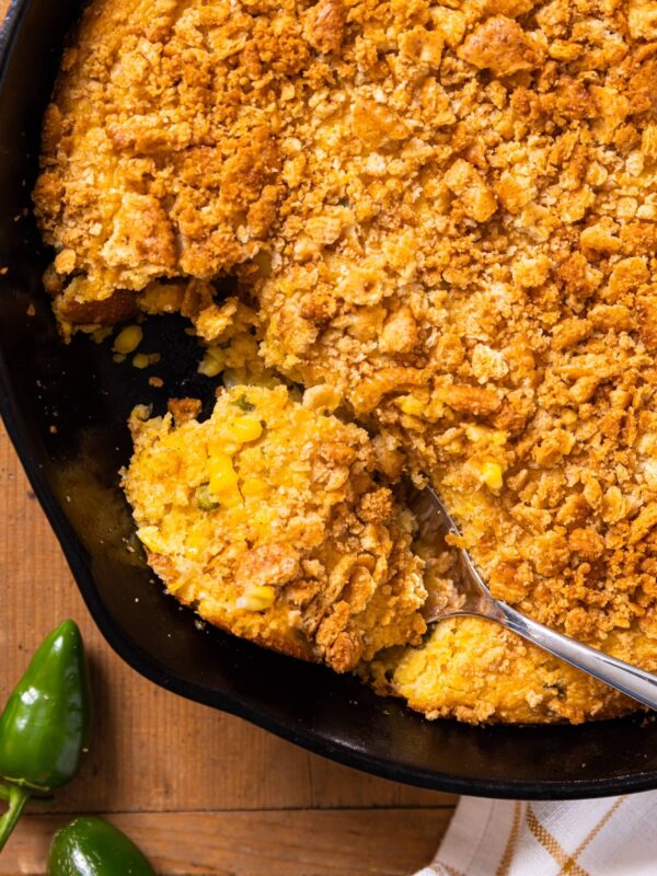 Top down view of black cast iron skillet sitting on wooden board filled with brown colored spoon bread mixture