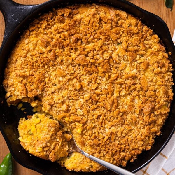 Top down view of large black cast iron skillet holding golden colored corn spoon bread sitting on wooden board