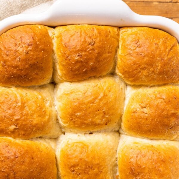 Top down view of golden dinner rolls sitting in white baking dish on wooden board with pot holders underneath