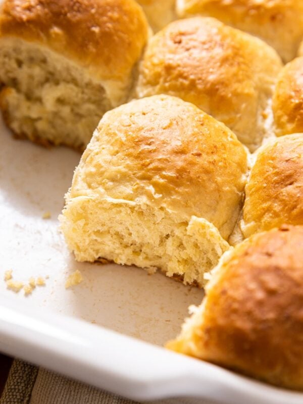 Lightly golden brown dinner rolls sitting in white pan after coming out of the oven with several rolls missing