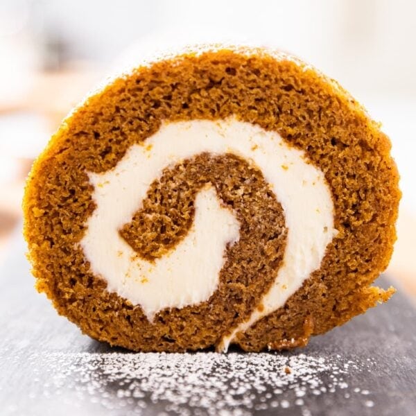 Side view of pumpkin roll with rings of cream cheese and pumpkin cake sitting on piece of slate on countertop