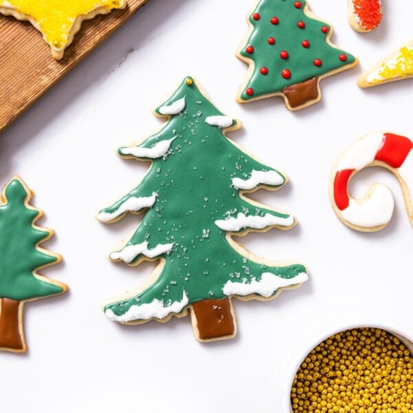 Decorated Christmas tree sugar cookie sitting on white countertop with other cookies all around
