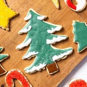 Top down view of wood cutting board sitting on white countertop with decorated sugar cookies on top in all kinds of colors