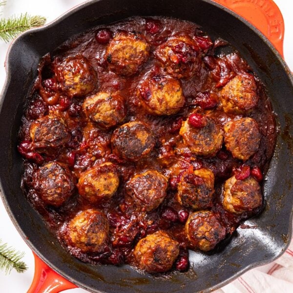 Red skillet sitting on white countertop filled with cranberry sauce covered meatballs