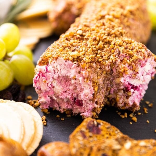 Cranberry cheese log sitting on piece of slate with grapes and crackers all around