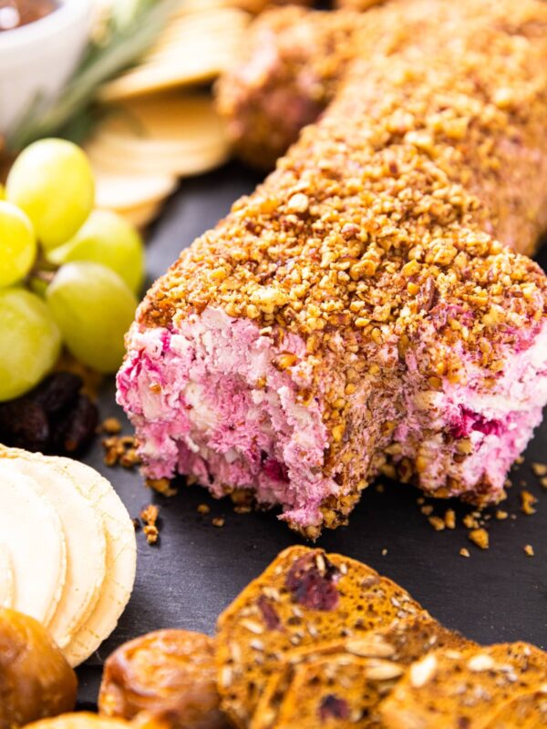 Cranberry cheese log topped with chopped pecans sitting on slate board with crackers and grapes sitting around