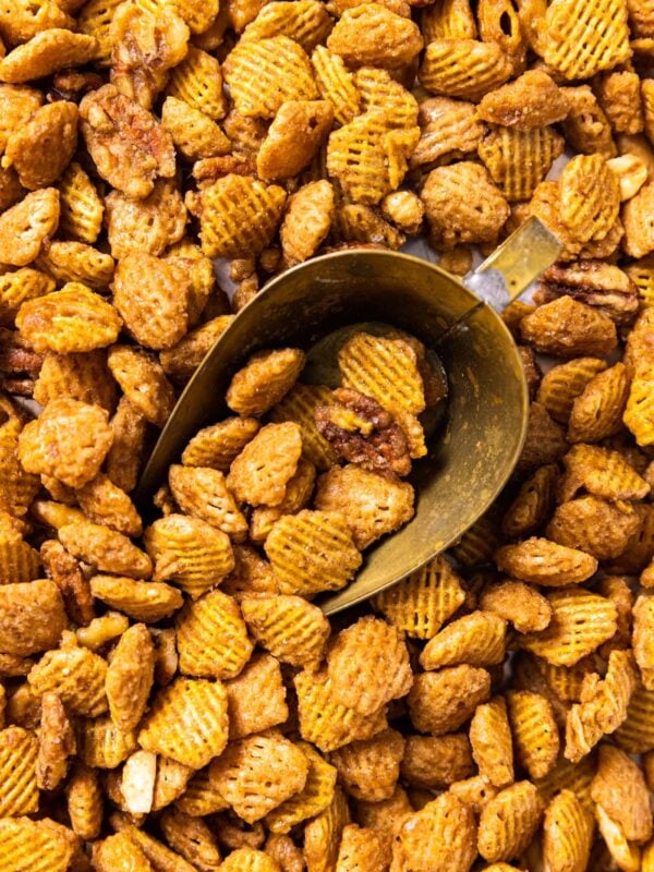 Top down view of sweet glazed party mix sitting on sheet pan with brass scoop amongst the rice cereal and nuts