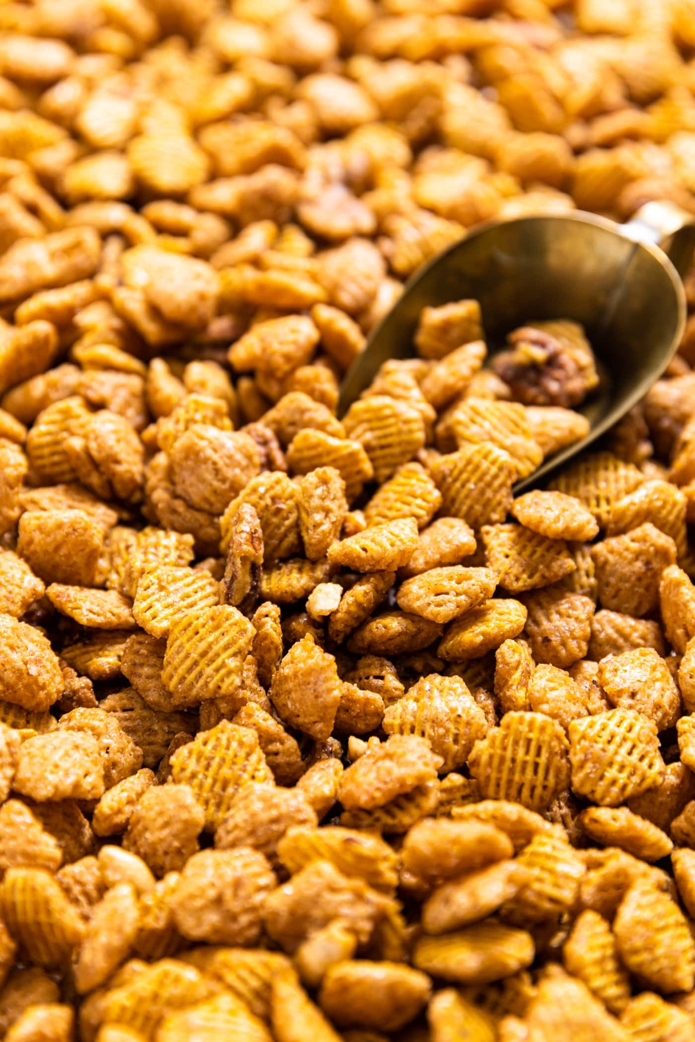 Sheet pan filled with sweet glazed party mix with rice cereal and nuts with scoop sitting in background