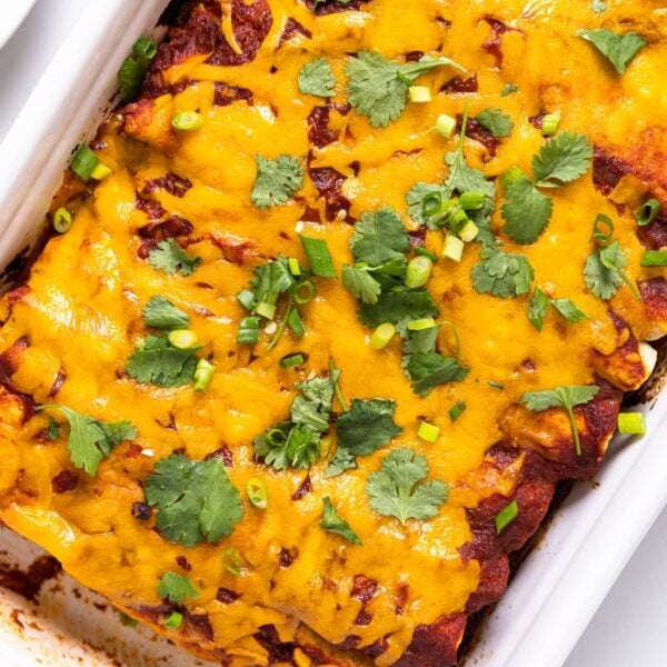 Top down view of white baking dish filled with chicken enchiladas topped with cheese and cilantro all sitting on white countertop
