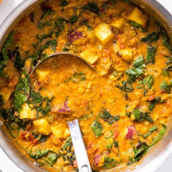 Top down view of metal kettle filled with orange colored lentil soup with ladle sitting in middle of soup all on white countertop