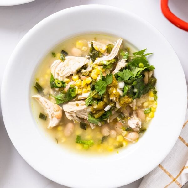 Top down view of white bowl filled with white bean chicken chili sitting on white countertop with napkin and silverware