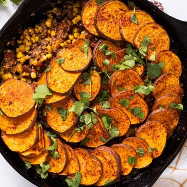Top down view of sweet potatoes shingled over taco bake with cilantro sprinkled over the top in a black skillet