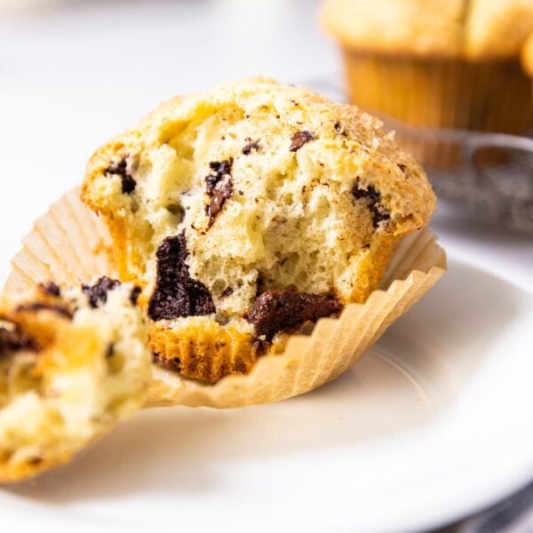 Chocolate chunk muffin sitting on white plate with more muffins in background all on white countertop