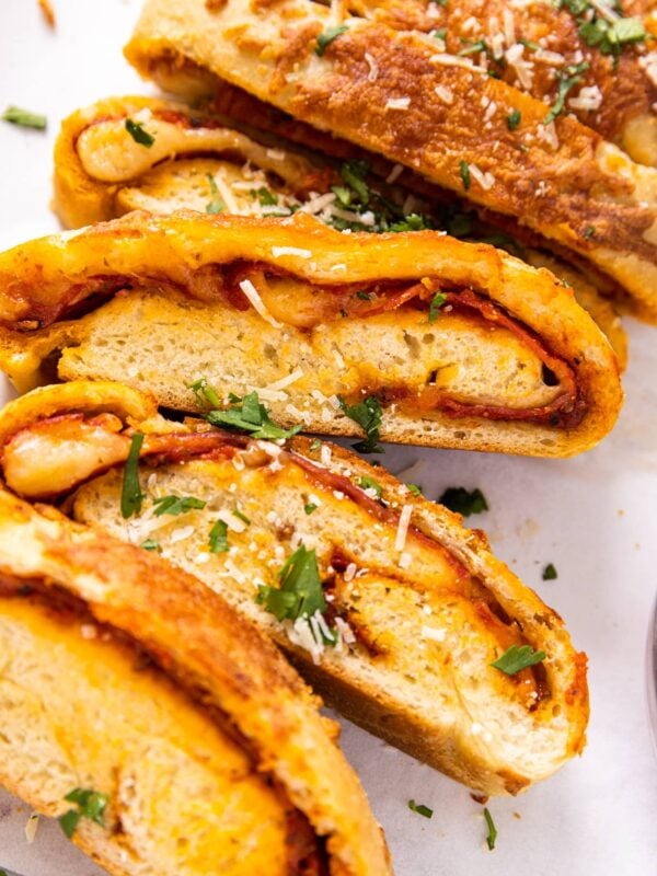 Slices of stromboli sitting up against each other all on white piece of parchment paper with parsley and Parmesan cheese sprinkled on top