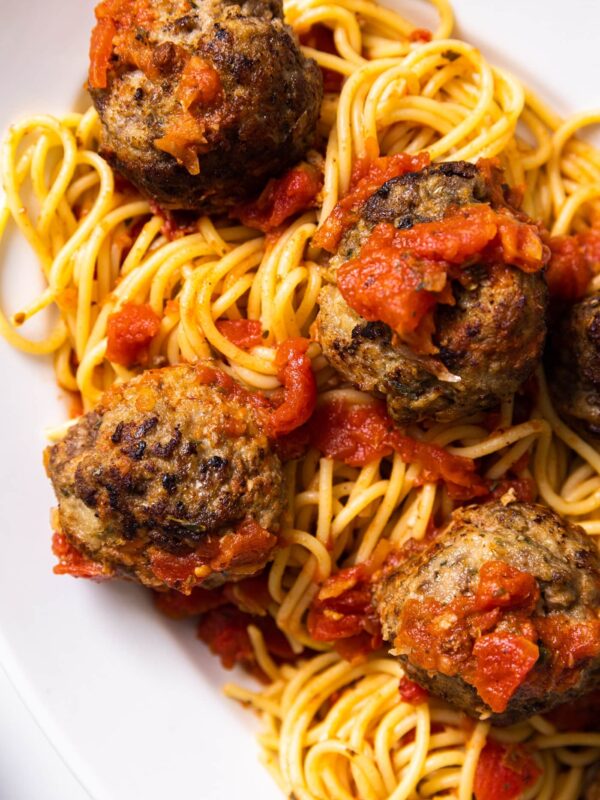 Top down view of white plate filled with yellow colored spaghetti and topped with tomato sauce with meatballs intertwined