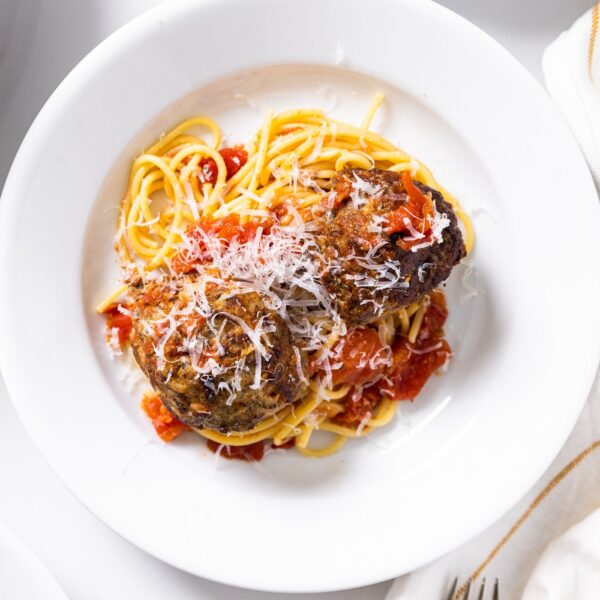 Top down view of white plate filled with spaghetti and meatballs sitting on white countertop with a white napkin