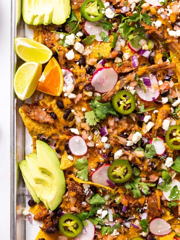 Top down view of metal sheet pan filled with tortilla chips and cheese and topped with pulled pork and other toppings