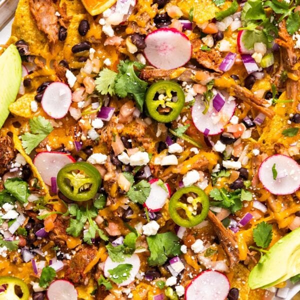 Top down view of metal sheet pan filled with tortilla chips and pulled pork with melted shredded cheese on top along with other toppings as well as avocado