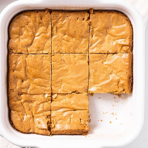 Top down view of white baking dish filled with golden colored brown butter blondies with nine squares cut