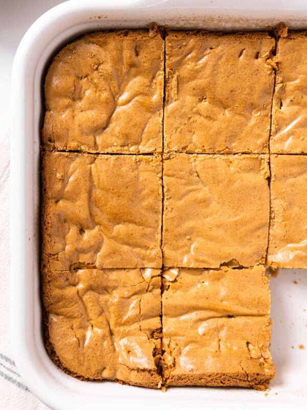 Top down view of golden colored blondies sitting in white baking dish after being baked with nine slices cut in squares