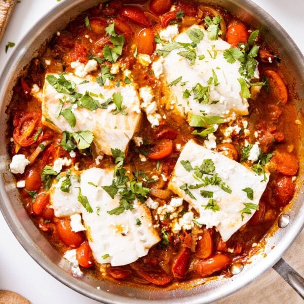 Top down view of metal skillet sitting on white countertop filled with red colored tomato sauce with pieces of cod sitting among the sauce topped with chopped cilantro