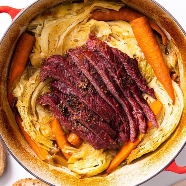 Top down view of red Dutch oven filled with yellow cabbage and carrots and red colored corned beef all on white countertop