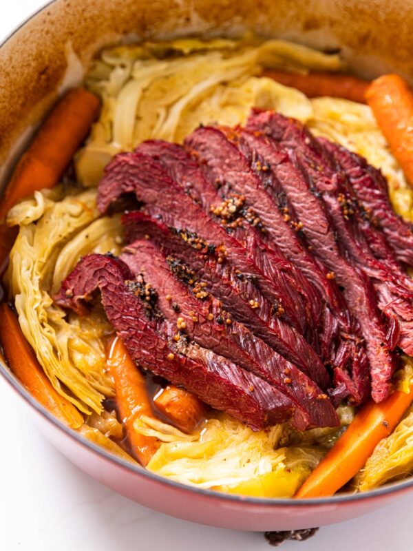 Red Dutch oven sitting on white countertop filled with yellow colored cabbage and red colored corned beef