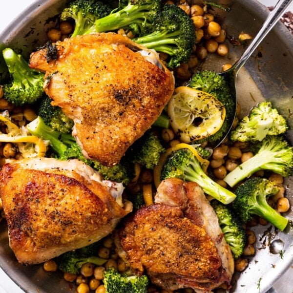 Top down view of metal skillet sitting on white countertop with three chicken thighs sitting on top of chickpeas and broccoli