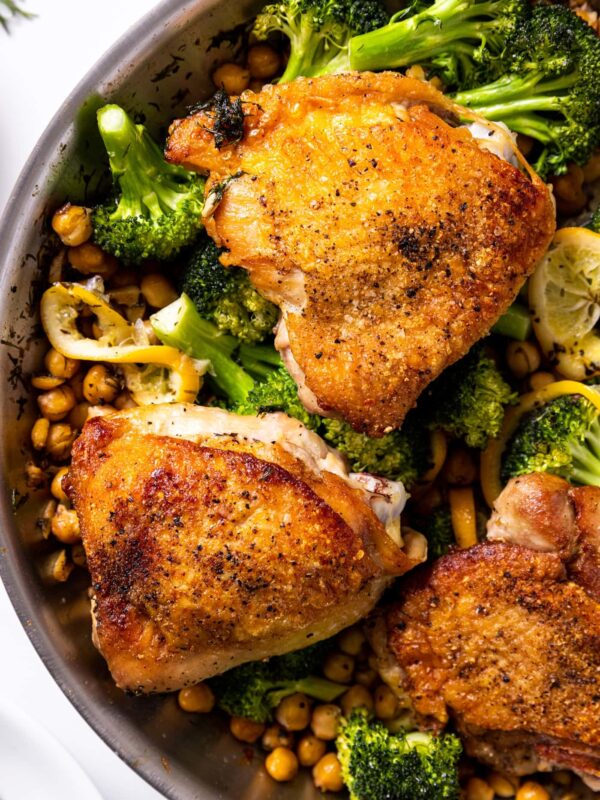 Top down view of skillet with browned chicken thighs sitting on top of chickpeas and broccoli with lemon slices
