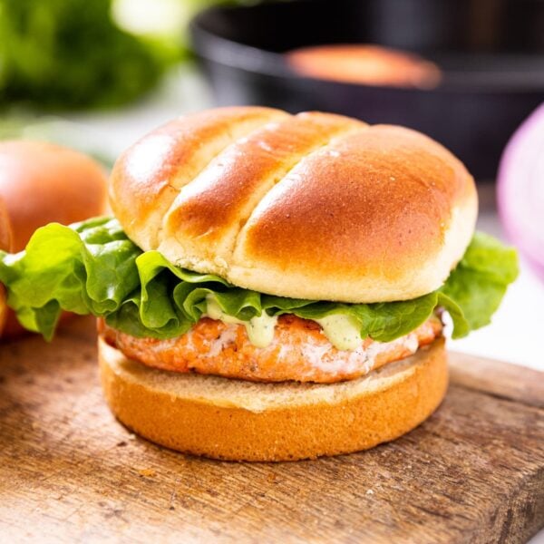 Salmon burger sitting on wood cutting board with brioche buns with black skillet in background as well as red onion