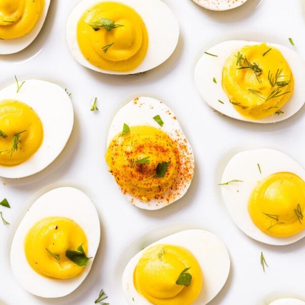 Top down view of white plate filled with deviled eggs filled with yellow colored creamy filling and topped with paprika and dill