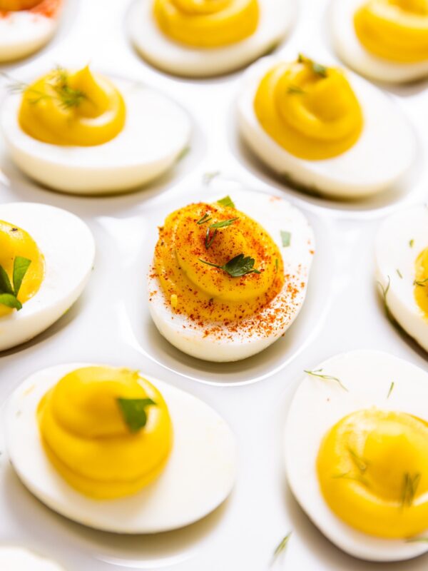 Hardboiled eggs sliced in half and filled with creamy filling sitting on white egg plate